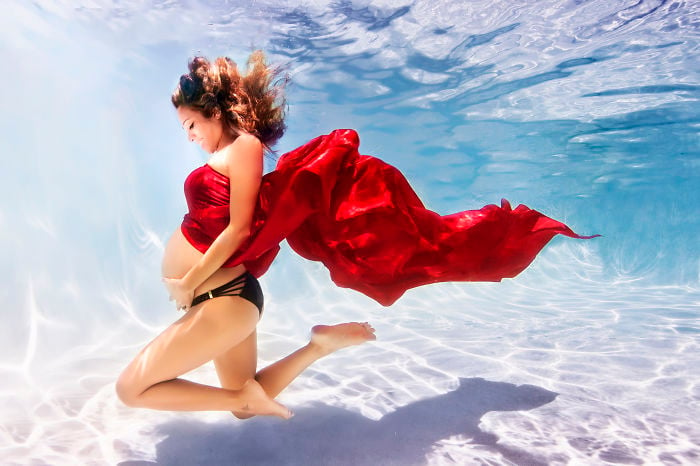 mujer embarazada bajo el agua vestida de rojo