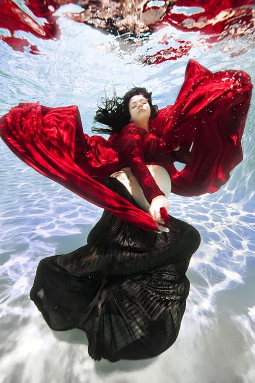 mujer embarazada bajo el agua vestida de rojo y negro