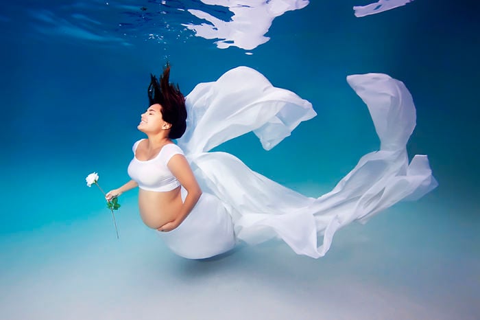 mujer embarazada bajo el agua vestida de blanco