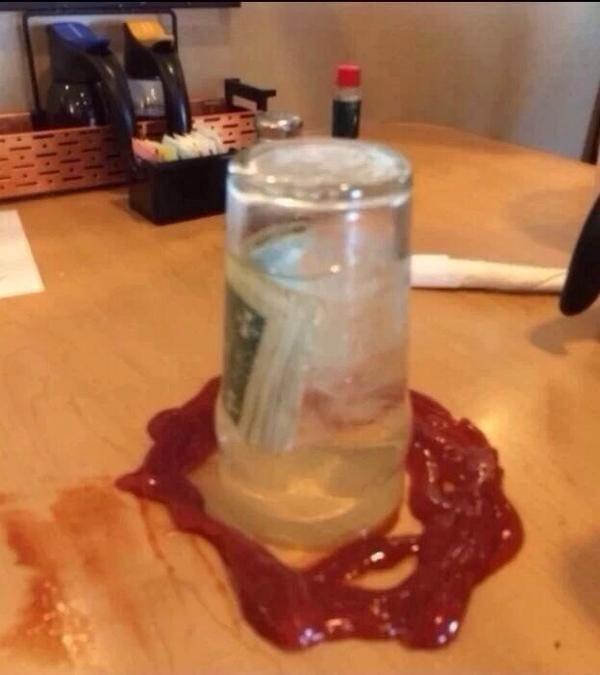 vaso invertido con agua y dentro un billete con el pago al restaurante alrededor esta con catsup