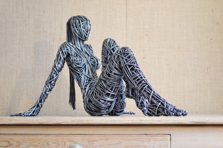 Escultura de una mujer sentada sobre un pedazo de madera 