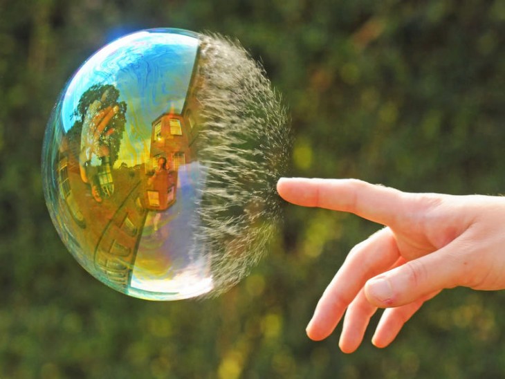 Imagen de una mano reventando una burbuja que pareciera que tiene photoshop