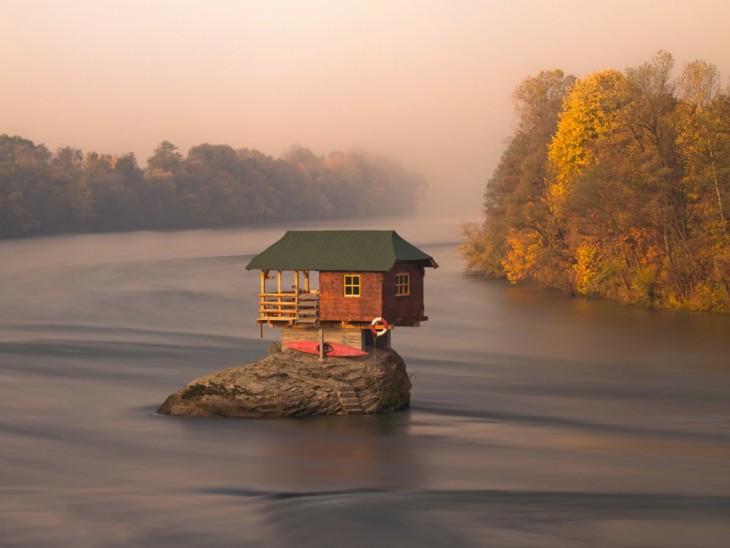 Fotografía de una casa construida en medio de un mar sobre una gran piedra 