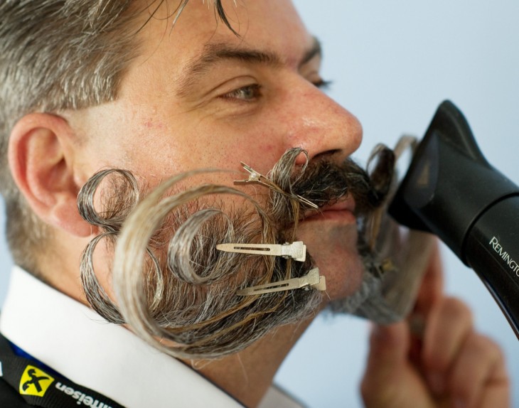 Cara de un hombre con una gran barba y bigote peinandose con una secadora de cabello 