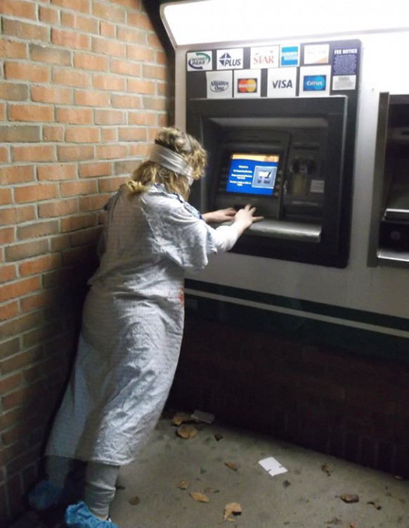 Mujer con bata de hospital y ojos vendados queriendo usar el ATM