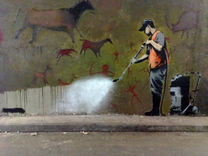 Grafiti de Bansky donde una persona esta aspirando pinturas rupestres de la pared 