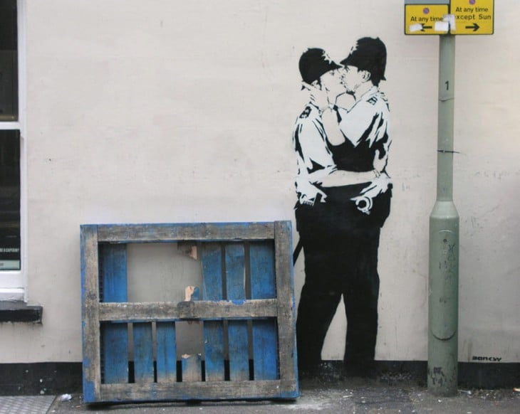 Grafiti de Bansky de dos hombres policías besándose en la boca 