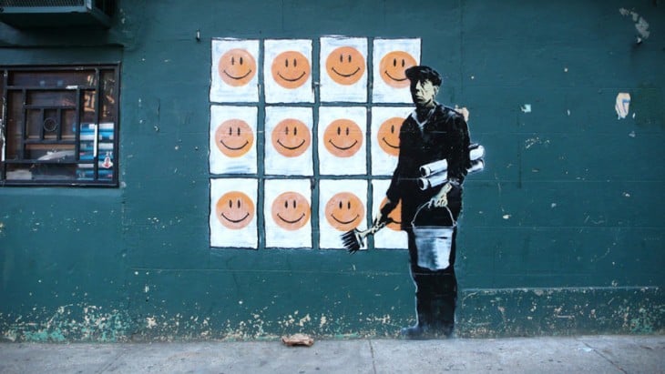 Grafiti de Bansky con un hombre con muchos cuadros de sonrisas 