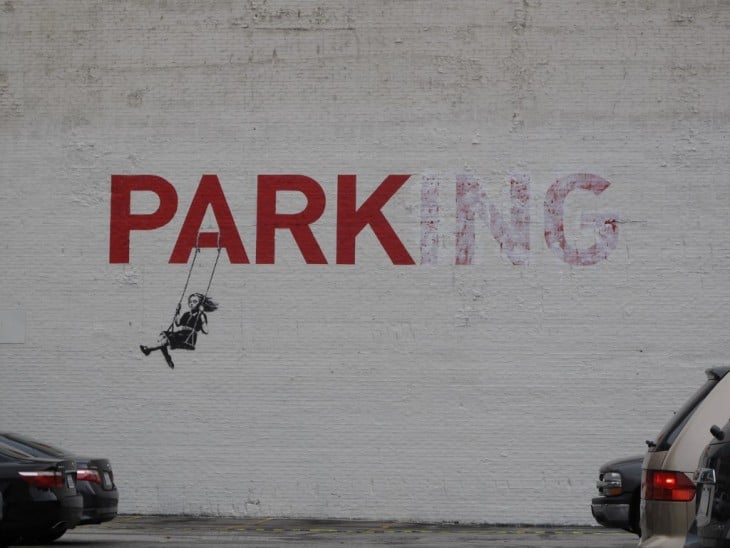 Arte urbana por Bansky de una niña columpiándose en la palabra Parking