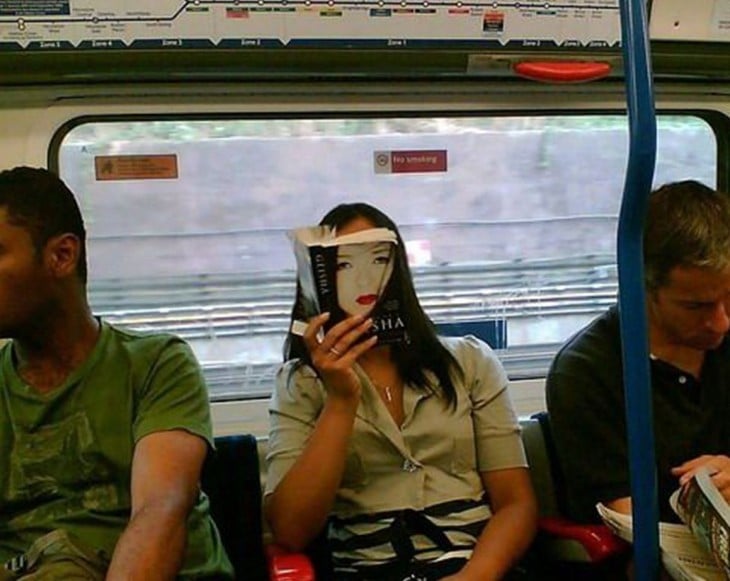 Mujer sentada en el transporte público con la portada de un libro frente a su cara 