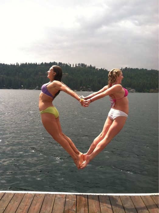 Dos chicas tomadas de las manos formando un corazón a punto de aventarse al agua 