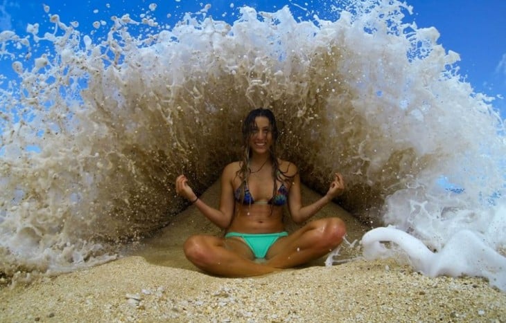 una chica sentada en la playa mientras una ola de agua pasa por encima de ella 