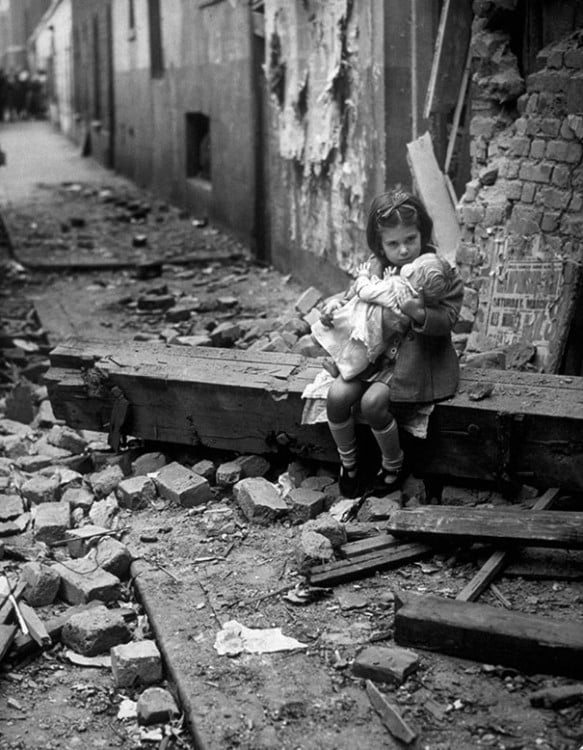 NIÑA SENTADA JUNTO A SU MUÑECA LUEGO DE UN BOMBARDEO