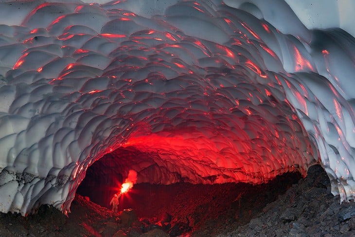 Hombre con una antorcha de fuego dentro de la cueva de hielo al volcán de Muntnovsky, Rusia