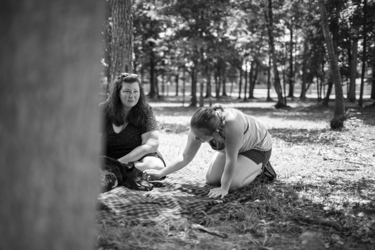 fotografía de dos mujeres cerca de un perro acostado en el suelo de un parque