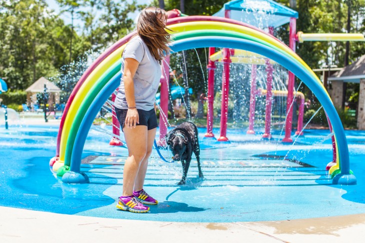 una chica mojándose con su mascota debajo de un puente de colores 