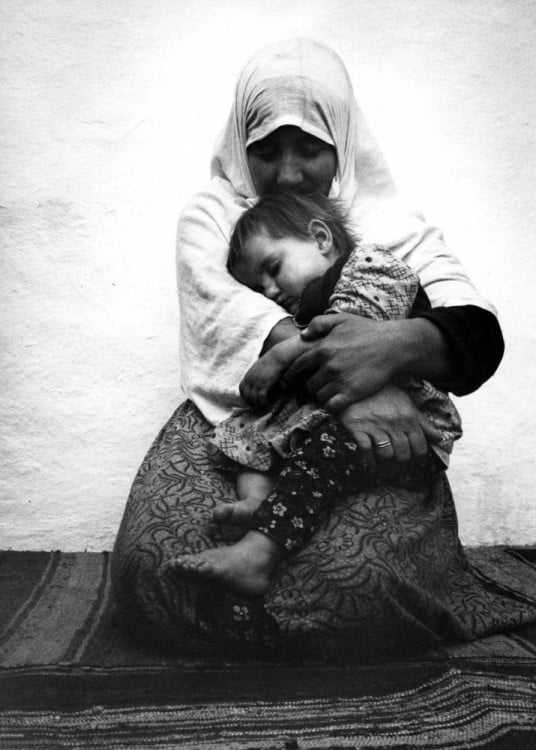 Mujer sentada en el suelo abrazando a su hijo mientras duerme 