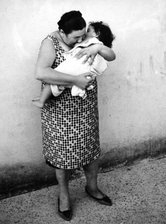 una mujer parada en la calle con su hijo en su brazos 