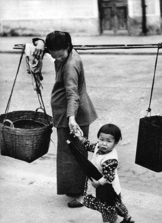 Mujer china cargando unas canastas y con un niño de la mano 
