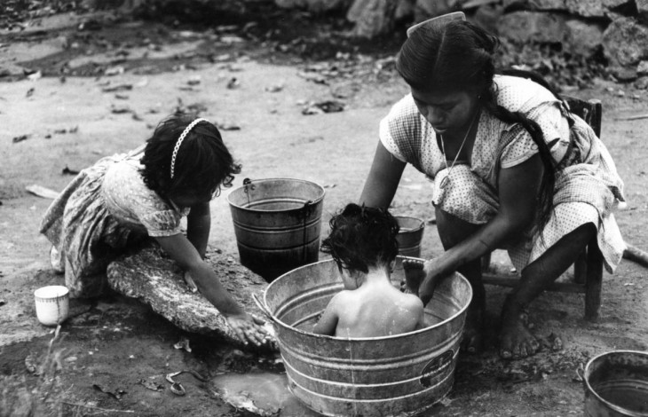 mujer bañando a su hijo dentro de una tina al aire libre 