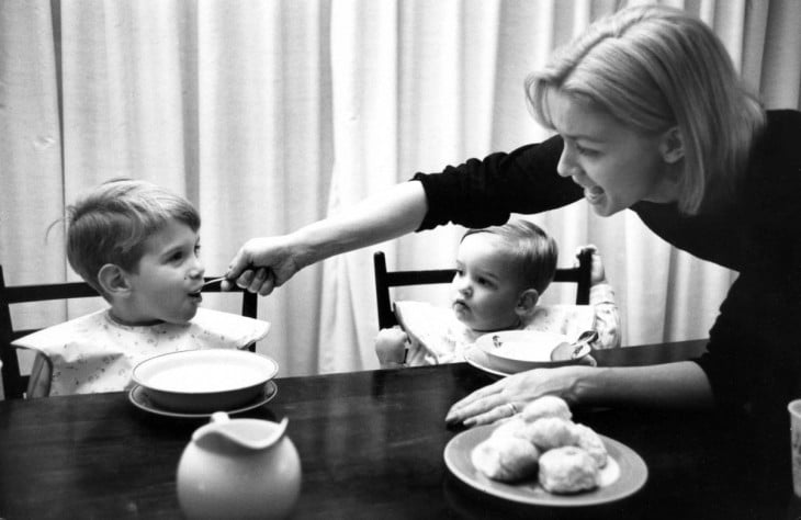 mujer alimentando a sus dos hijos en la mesa 
