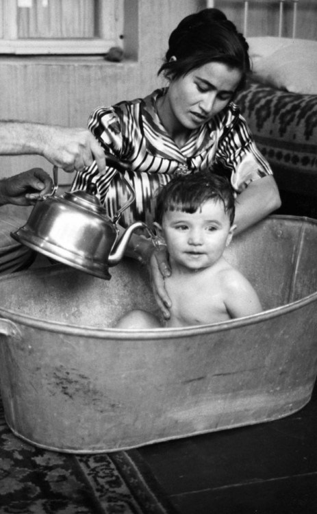 una madre bañando a su hijo dentro de una tina de aluminio 
