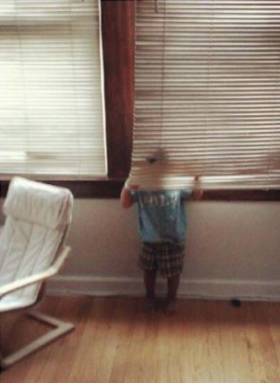 Niño escondido detrás de una persiana 