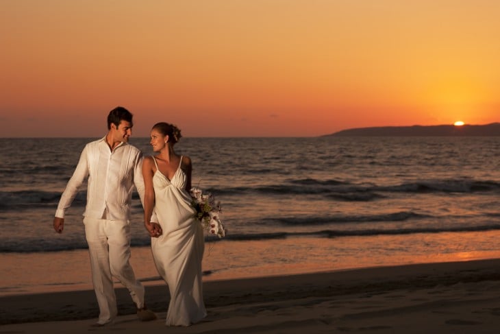 novios caminando por la arena del mar al atardecer