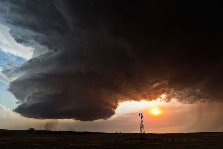 Paisaje con una enorme nube en forma de remolino y a lado el sol ocultándose 