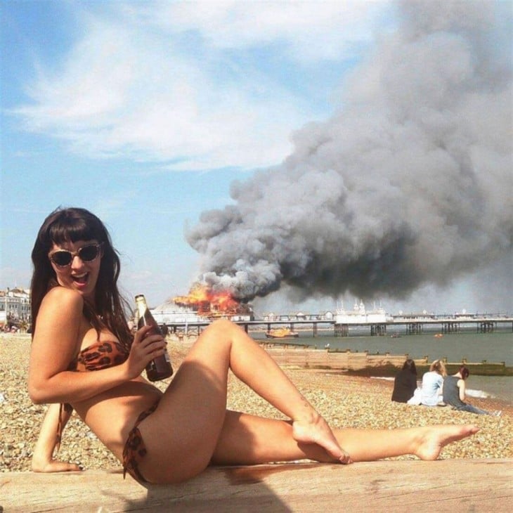 Fotogfrafía de una chica en traje de baño mientras detrás de ella un barco se quema 