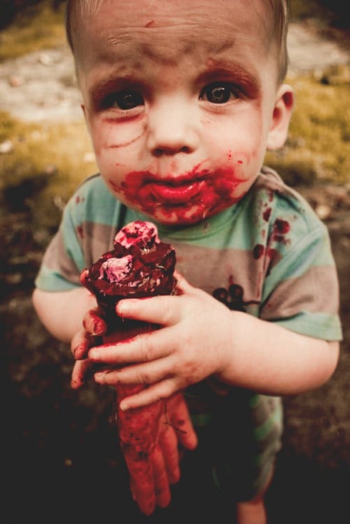 un pequeño niño disfrazado de Zombie simulando que se esta comiendo una mano 