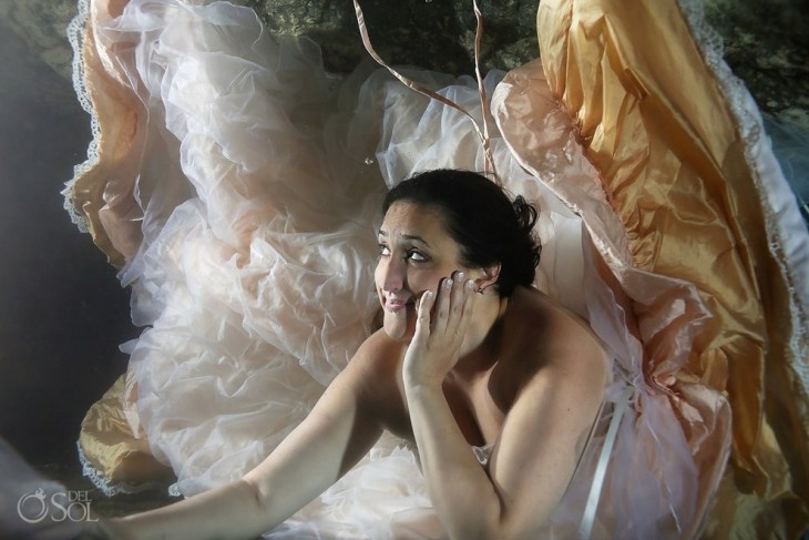mujer vestida de novia debajo del mar con una mano en la cara 