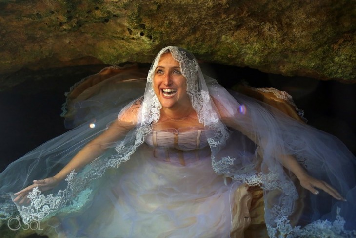 Mujer vestida de novia dentro del agua sonriendo y mirando hacia arriba 