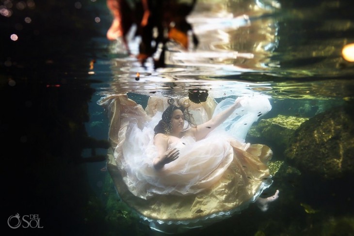 Chica vestida de novia sumergida en el agua entre rocas 