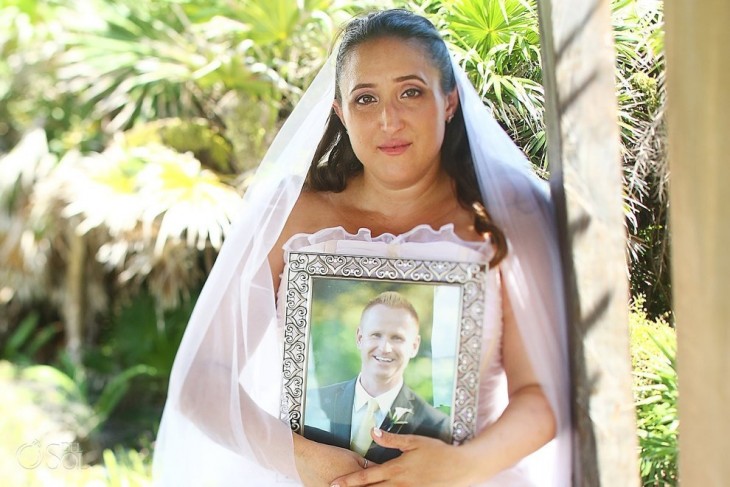 Mujer vestida de novia con la foto de su prometido recargada en su pecho 