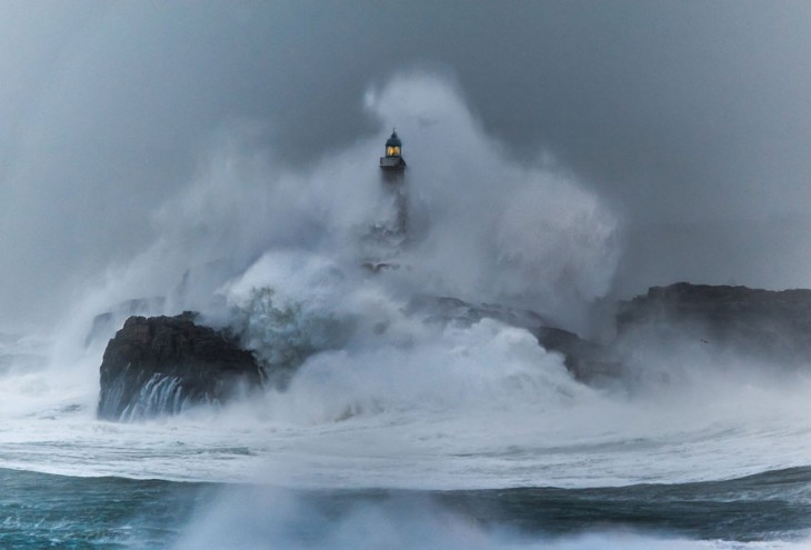 una ola gigante choca contra un faro