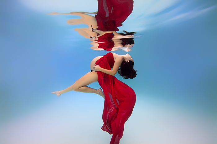 mujer embarazada bajo el agua vestida de rojo