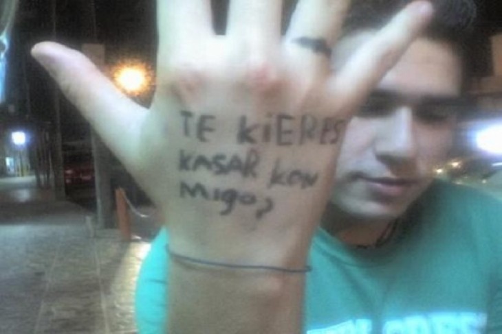 fotografía de un chico con la frase "te quieres casar conmigo" en una mano 