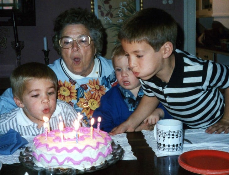 niño soplnado las velas de su pastel de cumpleaños acompañado de su abuela