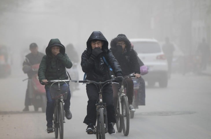 personas andando en bicicletas en medio de la polución en las calles de China