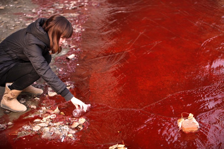 Reportera toma una muestras de agua roja contaminada del río Jianhe
