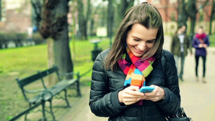 mujer que esta en un parque sonriendo al ver su celular