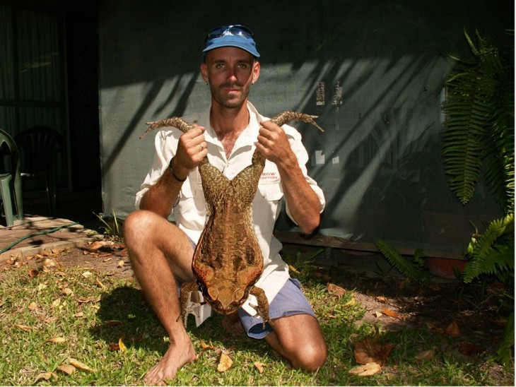 Un hombre sosteniendo de las patas a un sapo de gran tamaño 