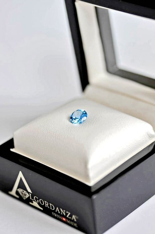 Estuche de la empresa Algordanza con un pequeño diamante azul en su superficie en color blanco 