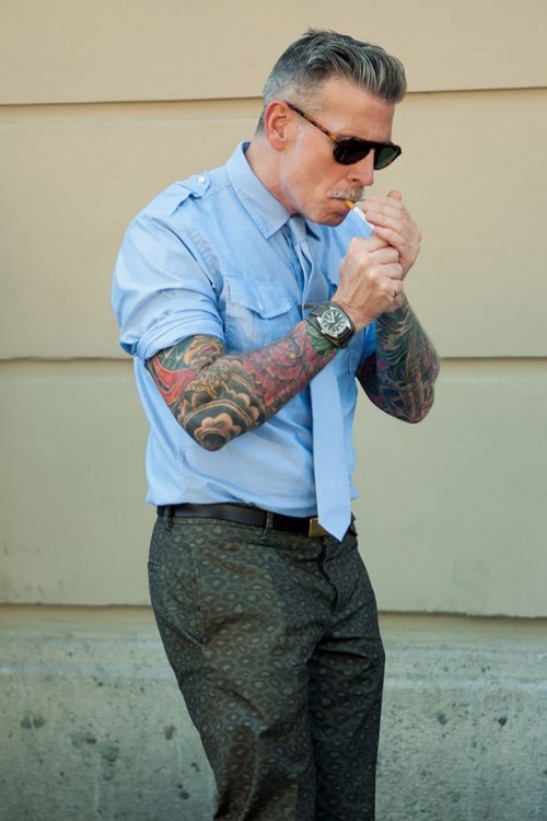 Hombre mayor y formal con tatuajes en los brazos prendiendo un cigarrillo 
