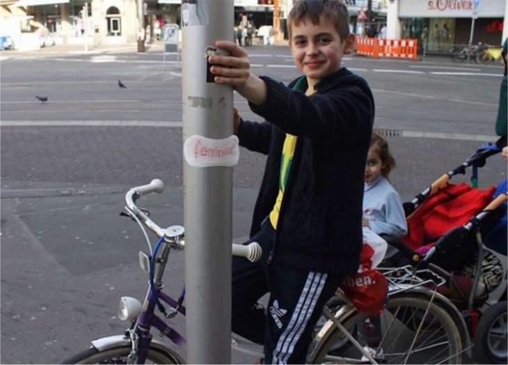Chico en bicicleta junto a una columna con una toalla femenina feminista