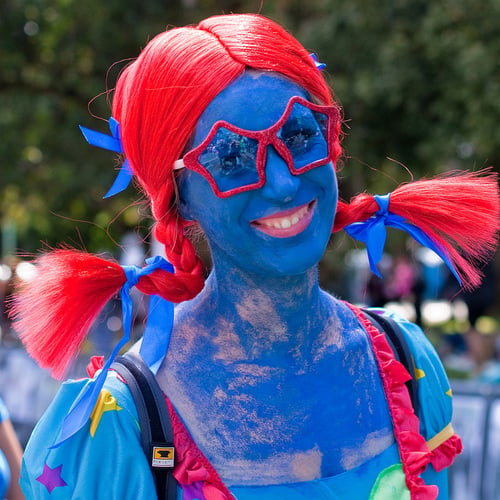 mujer con el cuerpo pintado de azul y peluca olor roja al igual que sus lentes 