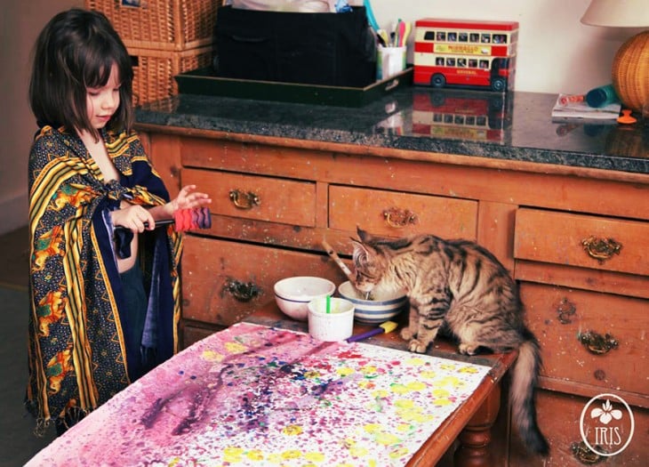 iris grace haciendo una pintura en su mesa junto a su gato 