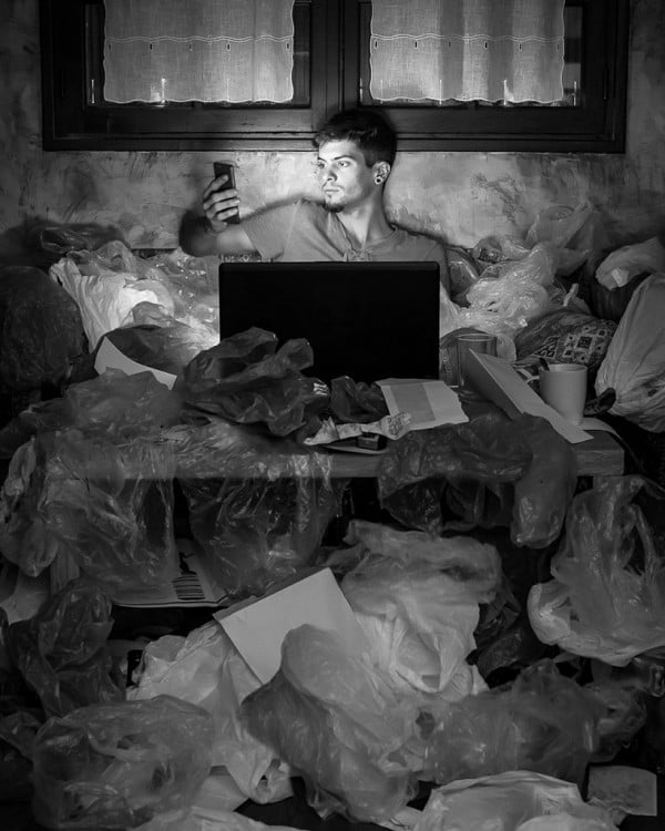 Hombre con celular y computadora rodeado de basura 
