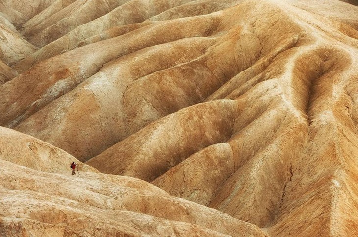 Hombre tomando una fotografía a unas montañas con algunas grietas y formas distintas 